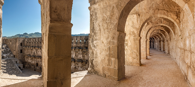 Panorama of top passageway in the theatre of Aspendos including arcade and a view of amphitheater and environs through space between columns. Aspendos amphitheater is remarkably well preserved part of ancient Pamphylian and later Greco-Roman city of Aspendos, now southern Turkey, Antalya province.
