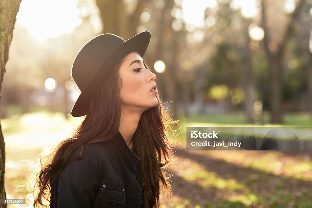 Thoughtful woman sitting alone outdoors wearing hat Portrait of thoughtful woman sitting alone outdoors wearing hat. Nice backlit with sunlight Adult Stock Photo