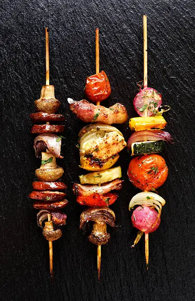 Photo of Grilled vegetable and meat skewers  on the black stone background