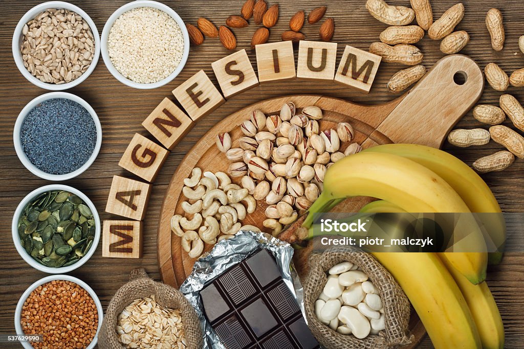 Products containing magnesium Products containing magnesium: bananas, pumpkin seeds, blue poppy seed, cashew nuts, beans, almonds, sunflower seeds, oatmeal, buckwheat, peanuts, pistachios, dark chocolate and sesame seeds on wooden table Magnesium Stock Photo