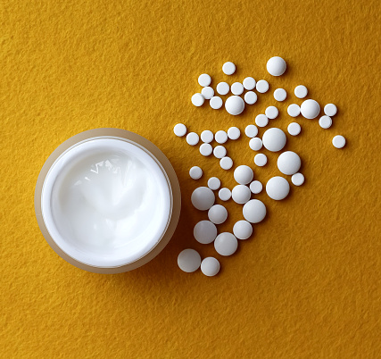 open cosmetic cream with pills on yellow background, flat lay