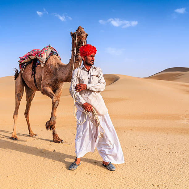 istock Indian man holding camel on sand dunes, Rajasthan, India 537637052