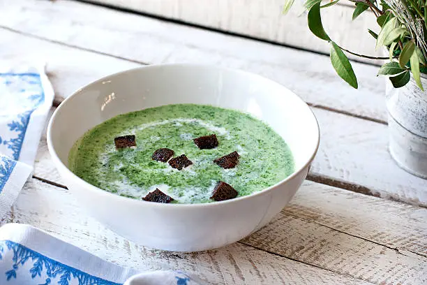 Spinach soup with croutons in bowl on wooden table