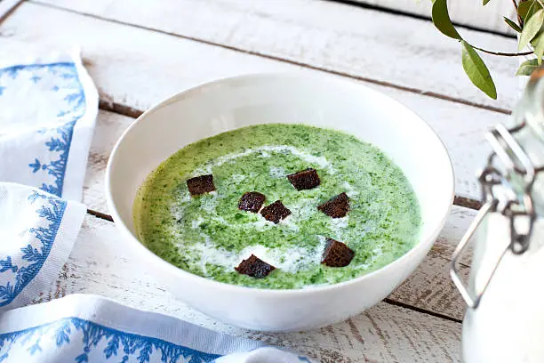 Spinach soup with croutons in bowl on wooden table