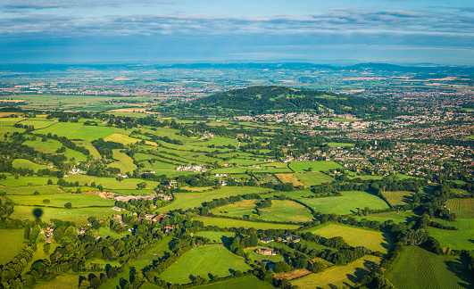 Aerial panoramic vista over the green patchwork landscape of the Cotswold escarpment, pasture and farms, to the City of Gloucester, the Severn Vale and Welsh mountains beyond. ProPhoto RGB profile for maximum color fidelity and gamut.