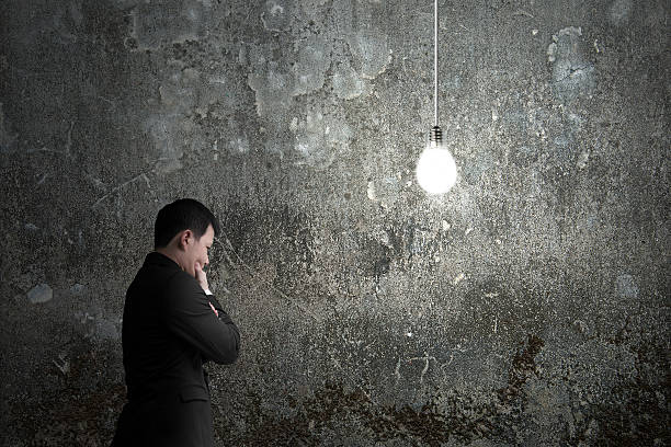 istock Businessman pondering with brightly light bulb illuminated dark 537663389