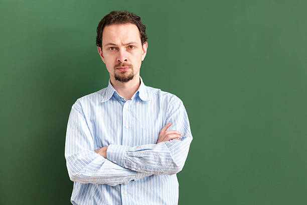 serious teacher standing with arms crossed at blackboard