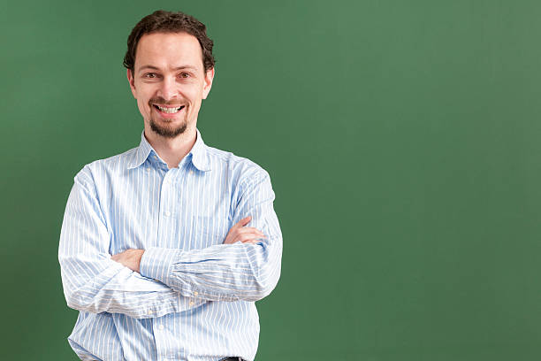 istock smiling teacher standing with arms crossed at blackboard 537665893