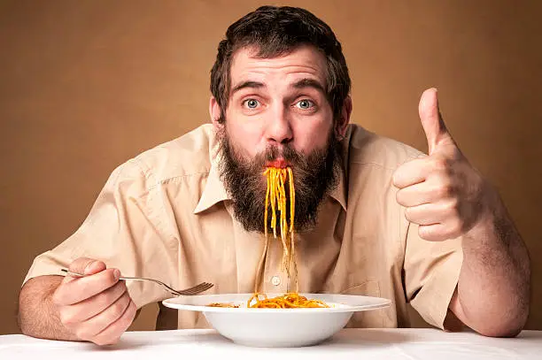 funny man with beard eating noodles showing thumb up - looking at camera 