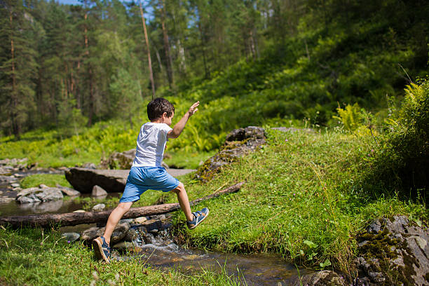 istock Little boy jumps over a stream in a forest 537685192