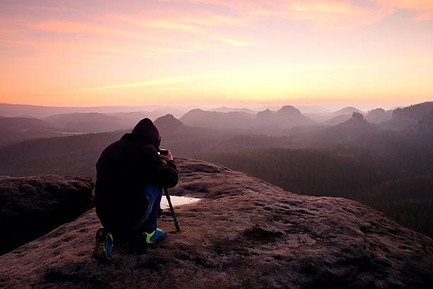 Professional photographer with tripod on cliff and work. Dreamy landscape