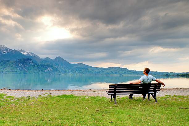 istock Alone  man sits on bench beside an azure mountain lake. 537687398