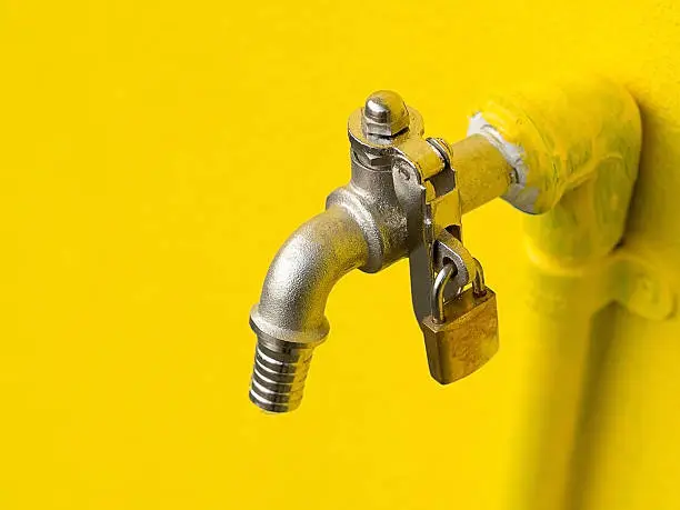 Photo of Yellow faucet on yellow wall with padlock prevent water theft