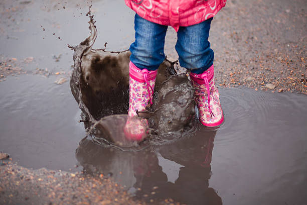 istock Child wearing pink boots jumping into a puddle 537688752