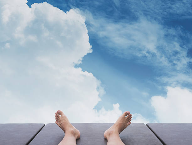 Male feet relaxing on sunbathing bed, with the sky