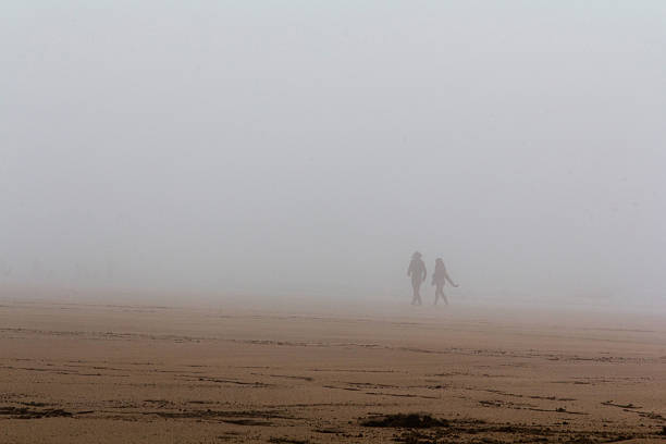 People walking along a mist covered beach stock photo