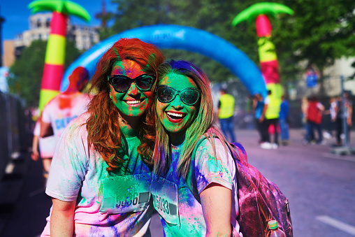 friends enjoying holi color festival in summer day, looking at camera and posing with colorful powder on their faces.