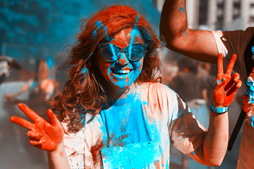 young woman showing peace sign at holi color festival, laughing and feeling amazing.