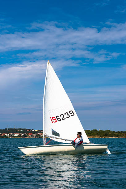 Young man sails a laser olympic  class sailing boat Side view of young male boats-man sailing on laser class sailing boat sailing dinghy stock pictures, royalty-free photos & images