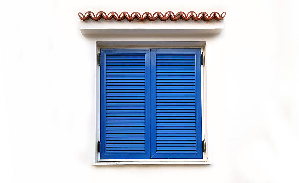 Window with closed blue shutters on white wall stock photo