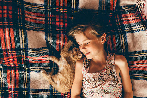 Little girl laying down near  the ginger kitten