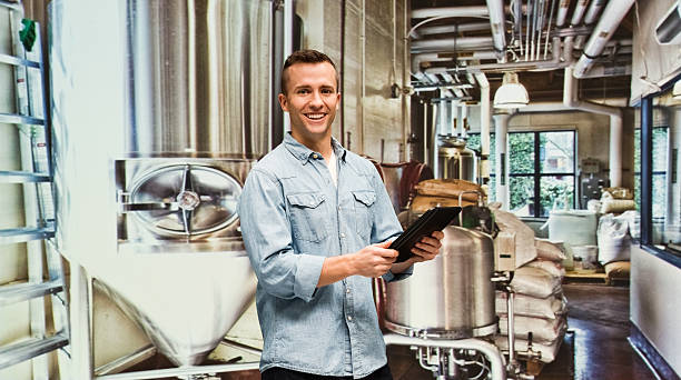 brewmaster sorridente utilizzando tablet in fabbrica - bottling plant brewery industry food foto e immagini stock