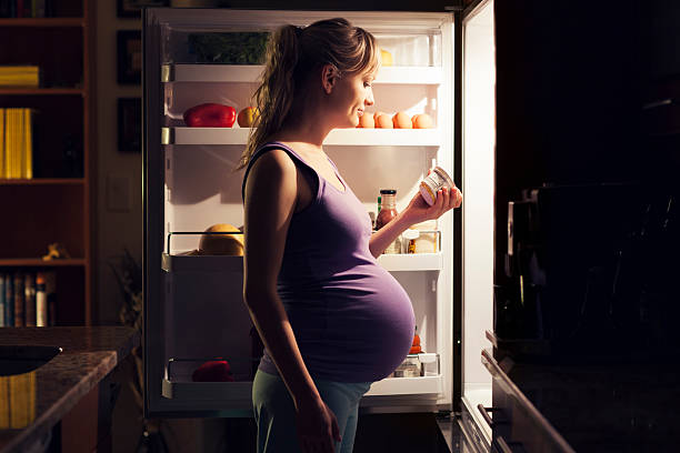 Pregnant young woman at refrigerator choosing healthy food stock photo