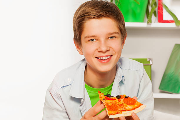 istock Happy boy holding pizza piece and eating at home 537699047