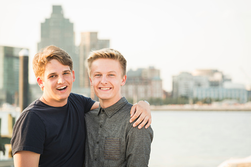 Two male gay friends pose for a photo at sunset overlooking the Baltimore Harbor.