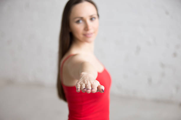 Beautiful happy young woman in bright colorful sportswear working out indoors in loft interior. Girl standing in Warrior 2 posture, Virabhadrasana Two pose. Close-up. Focus on the arm