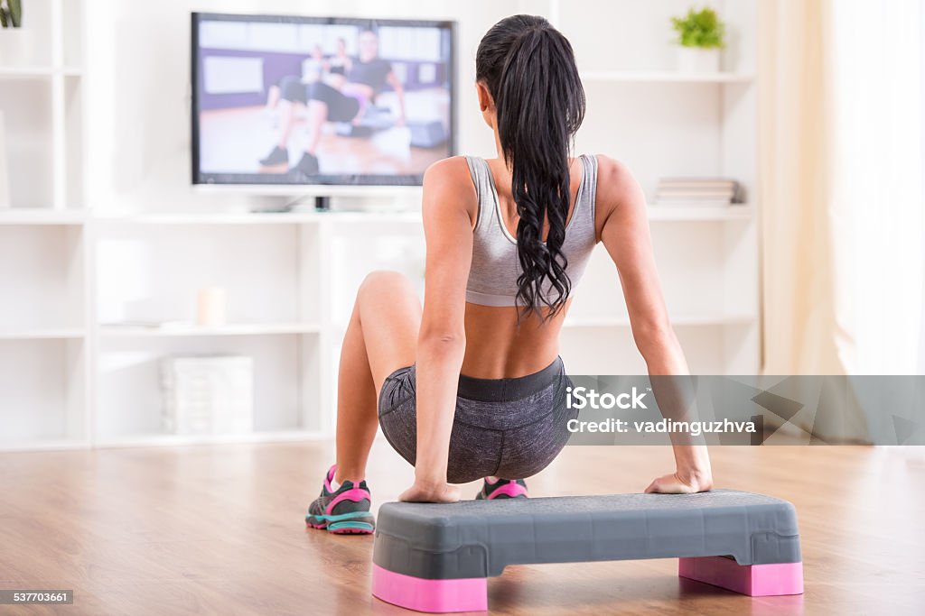 Fitness at home Rear view of a young woman doing home exercises while watching program on televisionYoung woman is exercising with dumbbells at home. Fitness, workout, healthy living and diet concept. 2015 Stock Photo