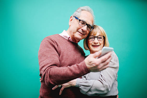 Senior couple in love Vintage toned image of a senior couple looking happy against a vibrant turquoise background, looking at the smartphone. Positive emotion, technology, progress, young at heart concepts. portrait of a smiling senior woman paris france stock pictures, royalty-free photos & images
