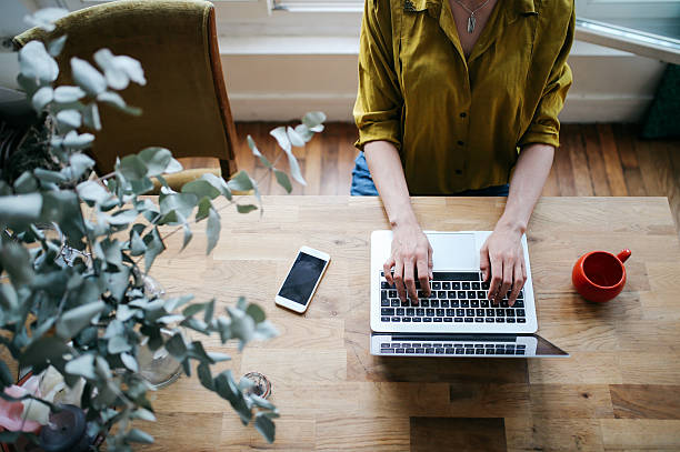 Overhead image of a female blogger writing on the laptop Overhead image of a female novelist, blogger, freelancer or a photographer, typing on the laptop keyboard in her living room in the beautiful bright apartment in Paris city center, in Montmartre district. She has a nice wooden retro table and a matching, vintage wooden floor. Retro processed with vibrant colors. Fashionable blogger, freelancer, work from home concepts in a laid back, cozy atmosphere in Paris, France. Paris Right Bank stock pictures, royalty-free photos & images