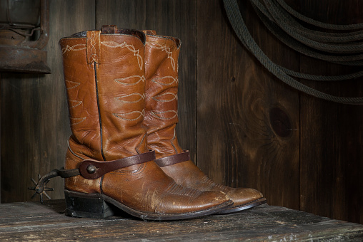 pair of light brown Cowboy boots in the barn on the shelf with rusty old spurs