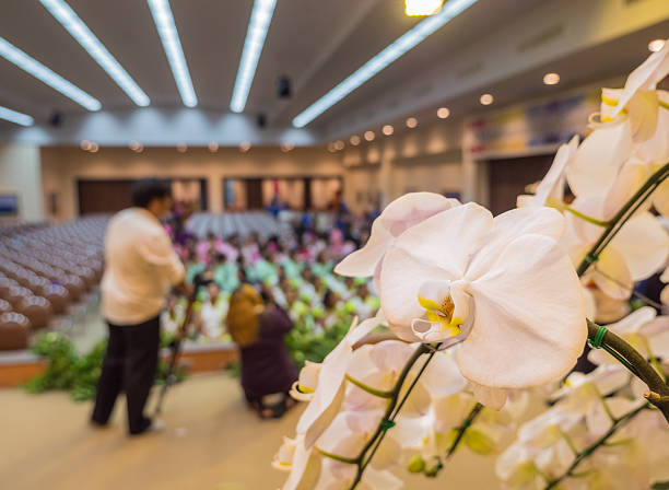 Selected focus at white orchid that decorate on state of big hall. Blur background of hall and people.
