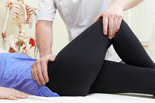 Male Osteopath Treating Female Patient With Hip Problem stock photo