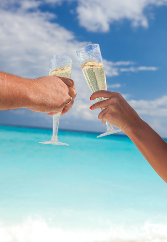 Clanging glasses with champagne at sandy beach and sea background, shallow depth