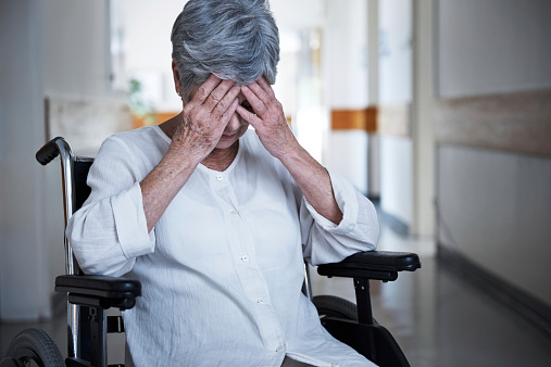 Shot of a senior woman in a wheelchair sitting with her hands over her eyes