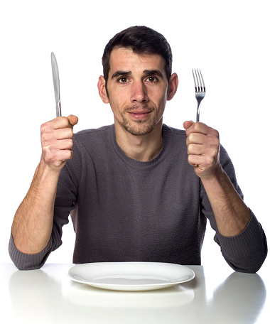 Man at dinner table with fork and knife raised. Hunger strike isolated over white background