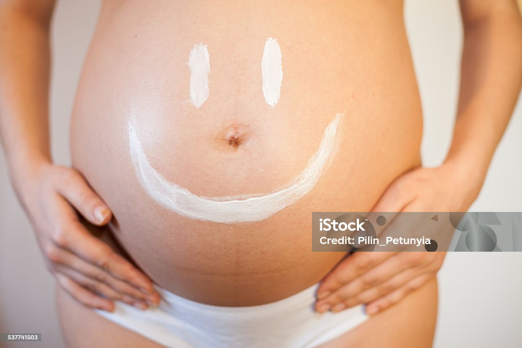 Pregnant woman with a smiley on her stomach Pregnant woman with a smiley on her stomach from the cream for the skin 30-34 Years Stock Photo