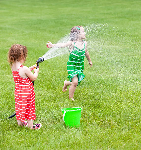 Two Girls Playing With Garden Hose in Summer