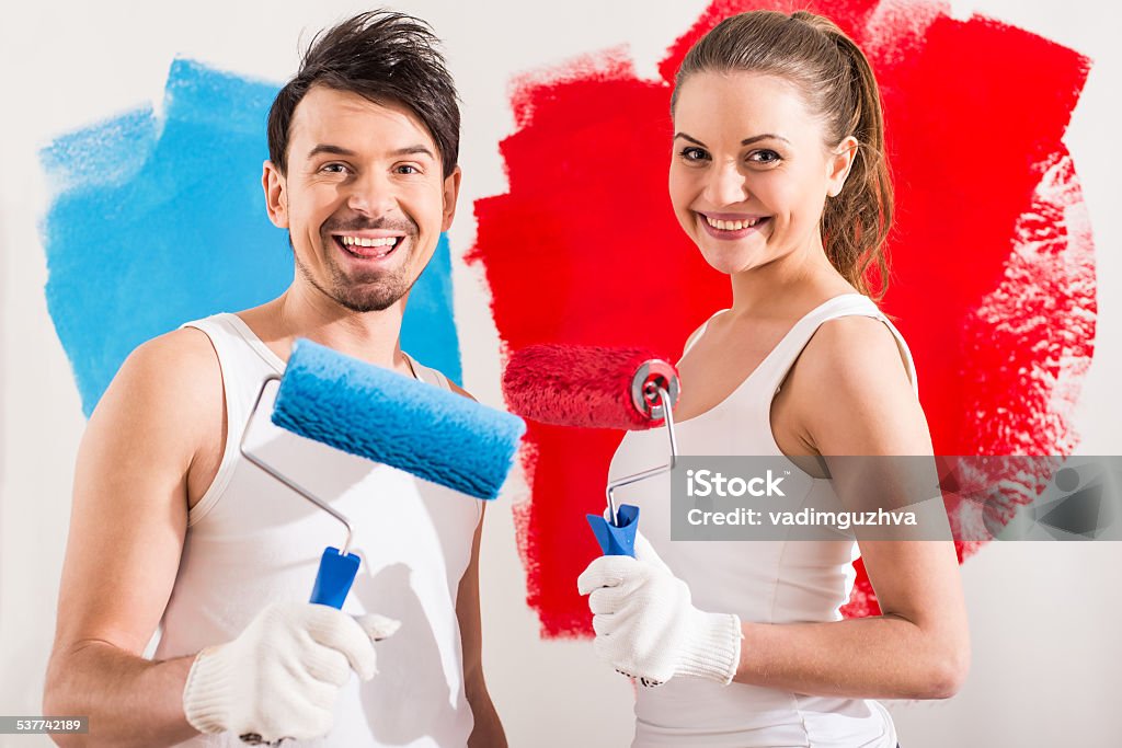 Repair home Young couple are doing repair at home and painting a wall with roller.Young, smiling couple are drilling a wall together. Young Women Stock Photo