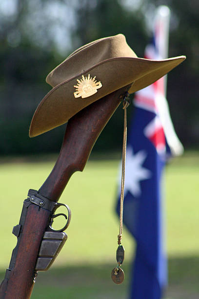 ANZAC Day - Closeup of Rifle, Hat, Flag and Dogtags Gold Coast, Australia - 25 April, 2010: Close-up image of an upturned, vintage Australian Army Lee Enfield 303 rifle, a soldier's dogtags and  Akubra slouch hat. The symbol of the Australian Army, the 'Rising Sun' badge can be clearly seen on the upturned brim of the iconic slouch hat.An Australian Flag can be clearly seen flying in the background during an ANZAC Day memorial service on the Gold Coast of Australia. larrikin stock pictures, royalty-free photos & images