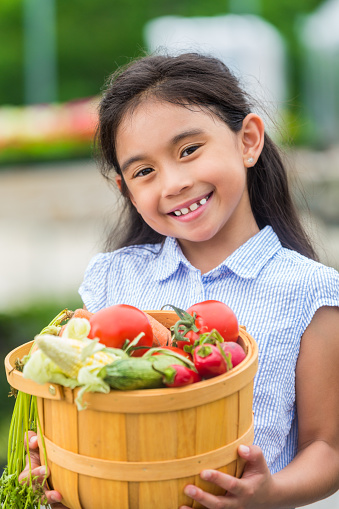 Pretty hispanic girl in blue holding basket of fresh vegetables.