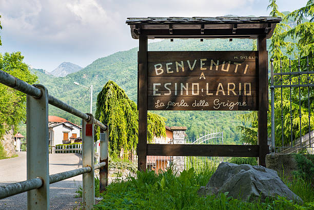 Esino Lario, Italy, tourist sign at the entrance of the village Esino Lario, province of Lecco, Italy - May 27, 2016: tourist sign at the entrance of the village. The sign says: "Welcome to Esino Lario the pearl of the Grigne." Esino Lario, venue between 21 to 28 June 2016 of the 12th international Wikimedia conference, is a small mountain village above Lake Como ; Grigne are a mountain massif near the village. In the background, at the bottom, you can see the first houses of Esino Lario wikipedia stock pictures, royalty-free photos & images