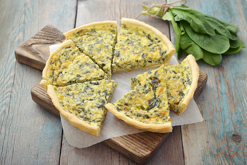 Traditional french quiche pie with spinach and cheese on wooden background