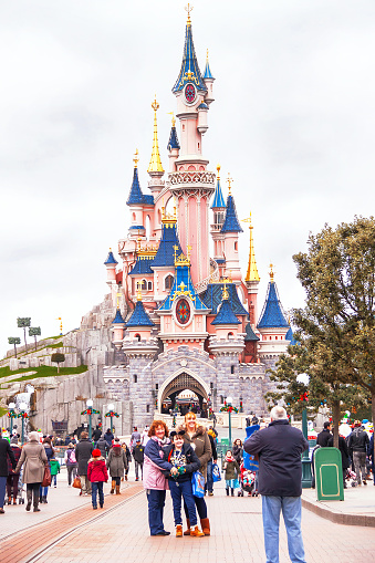 Paris, France - January 12, 2015: Happy people (family, child) near famous castle in the Disneyland Paris are taking photo. Disneyland is one of  the most popular destinations in Paris. Travel (vacation), entertainment, childhood concept. France. Europe.  