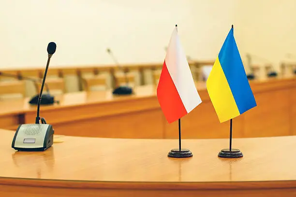 Table flags of Poland and Ukraine on the round wooden negotiating table with microphones.