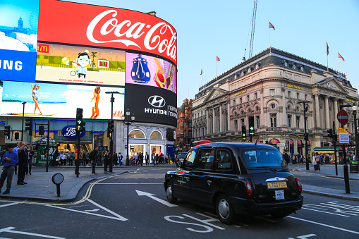 London, England - May 12, 2016: a black cab taxi crosses the iconic video advertising billboards of Piccadilly Circus, a famous public space in London's West End that was built in 1819 to join Regent Street with shopping Piccadilly Street