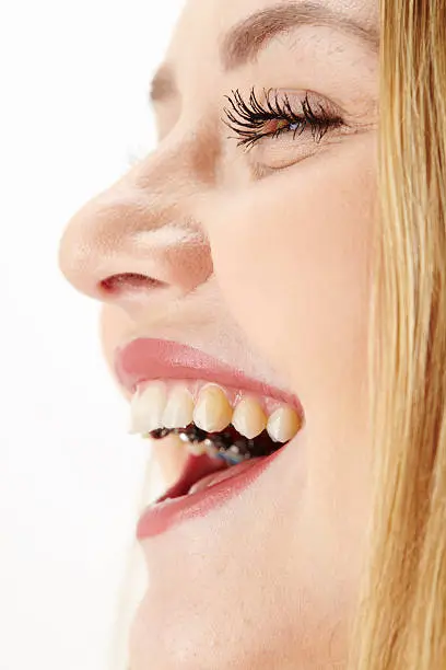 An attractive young blond woman laughs happy. The studio shot shows a crop of her face over white background.